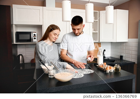 Couple preparing food together in a modern kitchen during the morning hours while smiling and enjoying each others company 136366769