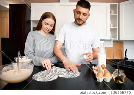 Couple prepares dough together in kitchen during morning time while making breakfast with eggs and milk on the counter 136366770