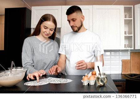 Couple prepares food together in kitchen while focused on recipe and ingredients in morning light 136366771