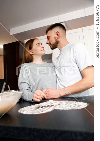 Couple shares a moment in the kitchen while preparing a dessert together during an evening at home in a cozy apartment setting Couple shares a moment in the kitchen while preparing a dessert together during an evening at home in a cozy apartment setting 136366775