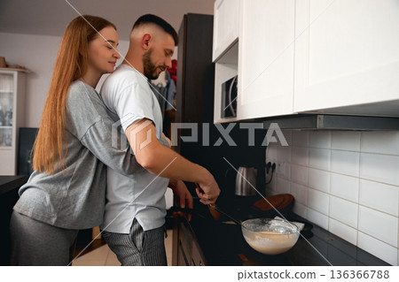 Couple is cooking together in a home kitchen while showing affection during the morning hours on a weekend 136366788