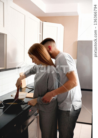 Couple cooking together in a modern kitchen during late morning hours while preparing a meal with simple ingredients and enjoying each others company Couple cooking together in a modern kitchen during late morning hours while preparing a meal with simple ingredients and enjoying each others company 136366794