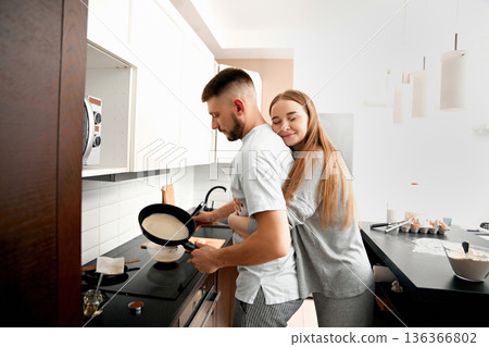 Couple cooking breakfast together in a modern kitchen during the morning hours Couple cooking breakfast together in a modern kitchen during the morning hours 136366802