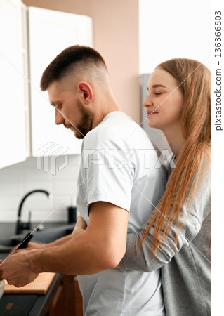 Couple cooks together in kitchen while sharing a warm moment in home setting during afternoon 136366803