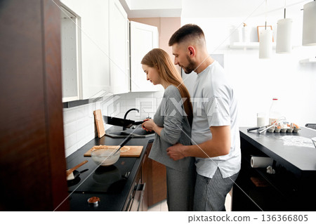 Couple cooking together in a modern kitchen while preparing a meal and enjoying each others company in the morning 136366805