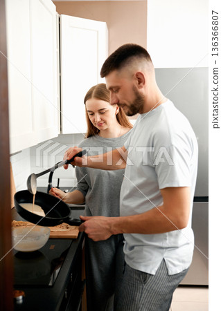 Couple cooks together in a kitchen while preparing breakfast on a weekend morning in a cozy home setting 136366807
