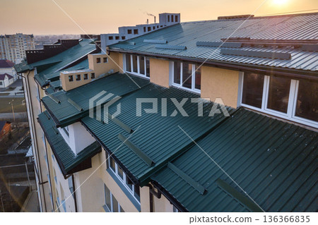 Aerial view of attic annex room exterior with plastic windows, roof and walls covered with green metal siding planks, new gutter system on top of high multi-storey apartment building. Aerial view of attic annex room exterior with plastic windows, roof and walls covered with green metal siding planks, new gutter system on top of high multi-storey apartment building. 136366835