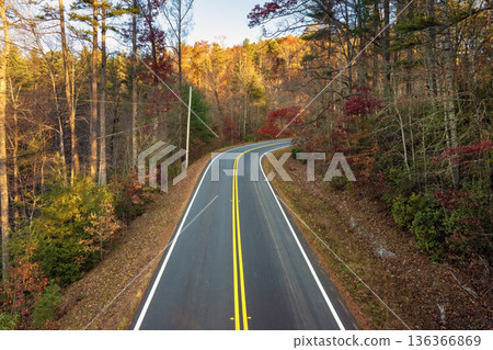 Car cruising on scenic road in Appalachian mountains at sunset. Trees glowing in vibrant fall foliage as the sun sets 136366869