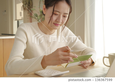 A woman managing her money by looking at her bankbook A woman managing her money by looking at her bankbook 136367599