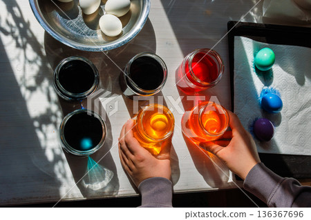 Top view of the hands arranging dye jars for easter egg coloring on sunlit table. 136367696