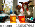 Sunlit kitchen craft scene with easter eggs soaking in a glass jars of yellow and orange food dye near a window 136367698