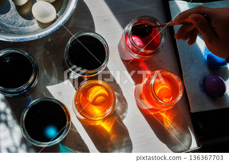 Spoon lifting pink dyed egg from jar in sunlit easter egg dyeing setup 136367703