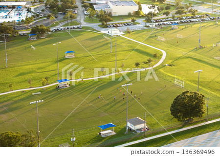 Aerial view of public sports park with children engaged in football game on grass stadium at sunset. Active way of life concept Aerial view of public sports park with children engaged in football game on grass stadium at sunset. Active way of life concept 136369496