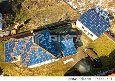 Aerial top view of new modern residential house cottage with blue shiny solar photo voltaic panels system on roof. Renewable ecological green energy production concept. Aerial top view of new modern residential house cottage with blue shiny solar photo voltaic panels system on roof. Renewable ecological green energy production concept. 136369521