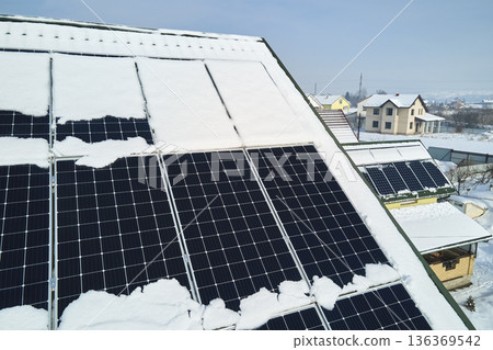 Aerial view of house roof with solar panels covered with snow melting down in winter end for producing clean energy. Concept of low effectivity of renewable electricity in northern region Aerial view of house roof with solar panels covered with snow melting down in winter end for producing clean energy. Concept of low effectivity of renewable electricity in northern region 136369542