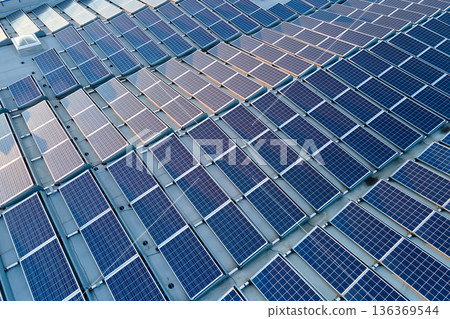 Aerial view of solar power plant with blue photovoltaic panels mounted on industrial building roof for producing green ecological electricity. Production of sustainable energy concept 136369544