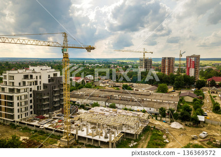 Aerial view of tower lifting crane and concrete frame of tall apartment residential building under construction in a city. Urban development and real estate growth concept. 136369572