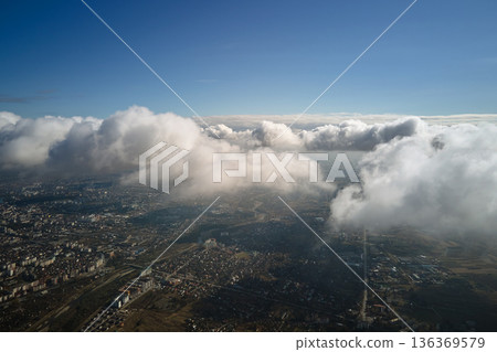 Aerial view from airplane window at high altitude of distant city covered with puffy cumulus clouds forming before rainstorm 136369579