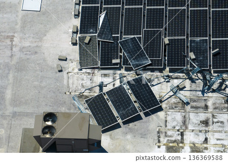 Top view of destroyed by hurricane Ian photovoltaic solar panels mounted on industrial building roof for producing green ecological electricity. Consequences of natural disaster in Florida 136369588