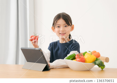 女孩拿著蔬菜,看著平板電腦 女孩拿著蔬菜,看著平板電腦 136370651