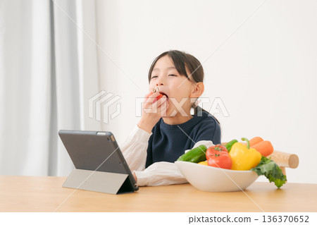 Girl holding vegetables while looking at tablet Girl holding vegetables while looking at tablet 136370652