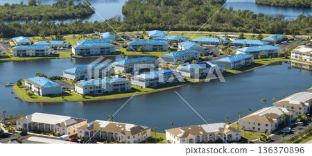 Hurricane damaged apartment buildings rooftops covered with protective plastic tarp against rain water leaking until replacement of asphalt shingles. Aftermath of natural disaster Hurricane damaged apartment buildings rooftops covered with protective plastic tarp against rain water leaking until replacement of asphalt shingles. Aftermath of natural disaster 136370896