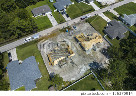 Aerial view of builders working on unfinished residential house with wooden roof frame structure under construction in Florida suburban area Aerial view of builders working on unfinished residential house with wooden roof frame structure under construction in Florida suburban area 136370914