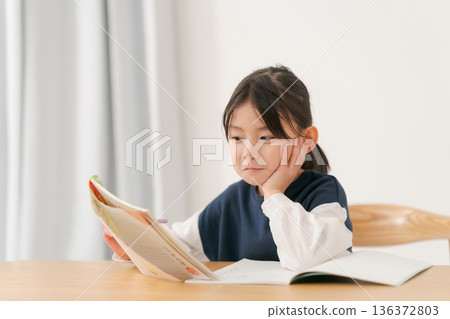 一個小學生女生正在學習,下巴托著手。 一個小學生女生正在學習,下巴托著手。 136372803