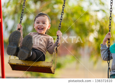 cheerful child girl playing on swing at playground 136372810