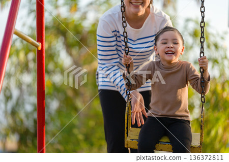 cheerful child girl with mother playing on swing at playground cheerful child girl with mother playing on swing at playground 136372811