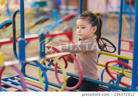 child girl playing with a steering wheel toy on playground 136372812