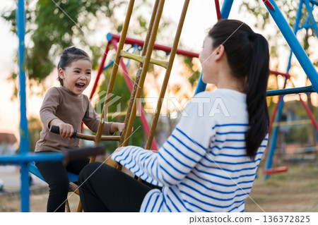 cheerful child girl playing on double swing with mother at outdoor playground cheerful child girl playing on double swing with mother at outdoor playground 136372825