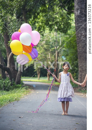 Vertical Cheerful beauty woman holding balloons relax sitting under big tree in green park with happiness. Woman Hands holding vibrant air balloons play birthday party summer time sunshine outdoor Vertical Cheerful beauty woman holding balloons relax sitting under big tree in green park with happiness. Woman Hands holding vibrant air balloons play birthday party summer time sunshine outdoor 136373216