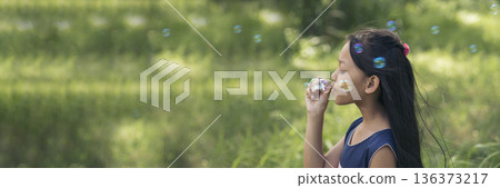 Adorable happy cute girl playful foam bubbles in green playground in summer outdoors. Funny Cheerful girl in the park happiness times. Bubbles blowing soap playful in nature park. Adorable happy cute girl playful foam bubbles in green playground in summer outdoors. Funny Cheerful girl in the park happiness times. Bubbles blowing soap playful in nature park. 136373217