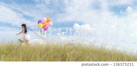Banner Cheerful cute girl holding balloons running green meadow white cloud and blue sky with happiness. Panorama Hands holding vibrant air balloons happy times summer sunlight outdoor copy space 136373231