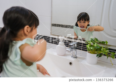 girl child brushing teeth and tongue at reflection in mirror in bathroom girl child brushing teeth and tongue at reflection in mirror in bathroom 136373266