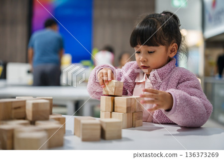 preschool child girl concentrating on building tower with wooden block 136373269