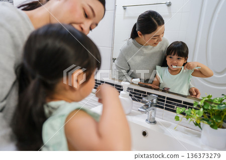 mother teaching girl child to brushing teeth at reflection in mirror in bathroom 136373279