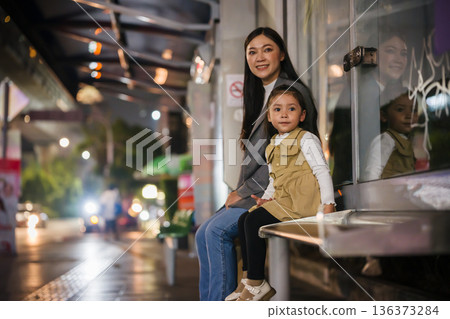 mother and child girl waiting for bus at bus stop in Bangkok city street at night, Thailand 136373284