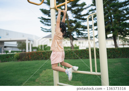 Young girl hanging on monkey bars in a sunny park, playground equipment, active childhood, outdoor fun, cheerful exercise, nature background, children's playtime 136373316