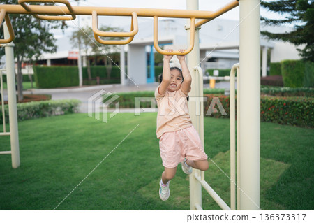 Happy child swinging on monkey bars in a playground, enjoying outdoor playtime and laughter during a sunny afternoon in a park setting 136373317
