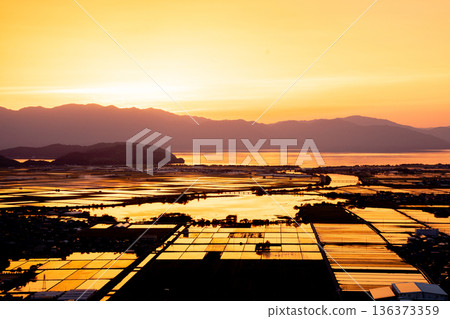 從滋賀縣東近江市豬子町的豬子山上眺望，傍晚時分，稻田在播種前的夕陽映照下泛著橙紅的光芒。 136373359