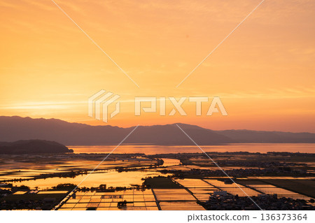 An evening view of flooded rice paddies glowing orange before planting, seen from Mt. Inoko in Inoko-cho, Higashiomi City, Shiga Prefecture 136373364