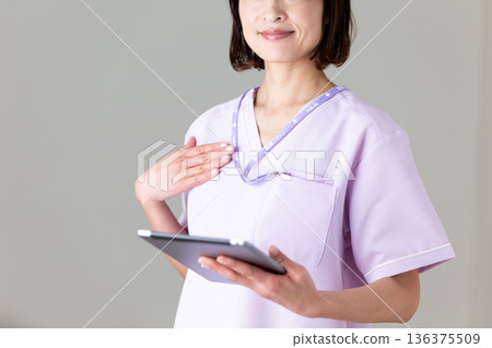 一位身穿醫用工作服的中年女護士，手裡拿著平板電腦 136375509