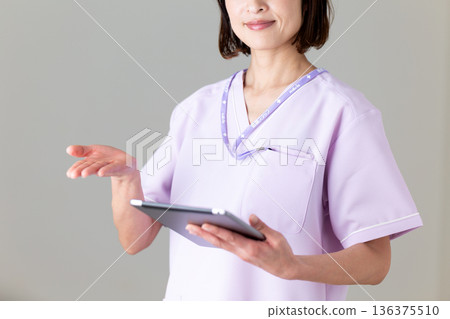 一位身穿醫用工作服的中年女護士，手裡拿著平板電腦 136375510