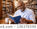 A man reading a book in a library 136376598