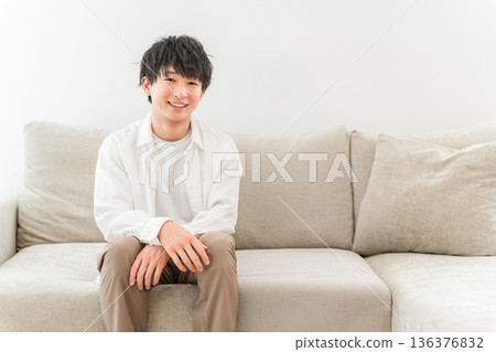 Smiling young Asian man sitting on a sofa in the living room at home 136376832