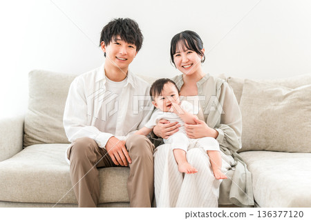 A young family sitting on a sofa and holding a baby, parent and child, family (childcare support, measures to combat declining birthrate) A young family sitting on a sofa and holding a baby, parent and child, family (childcare support, measures to combat declining birthrate) 136377120