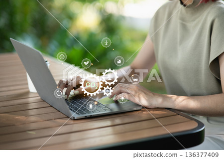 Woman using laptop with CO2 emission reduction and green energy icons. Concept of sustainability, net zero emissions, environmental conservation, and renewable technology for climate change. 136377409