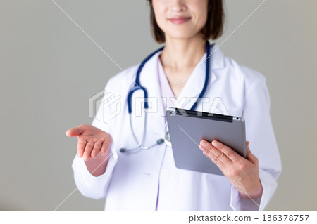 A middle-aged female nurse in a white coat holding a tablet A middle-aged female nurse in a white coat holding a tablet 136378757